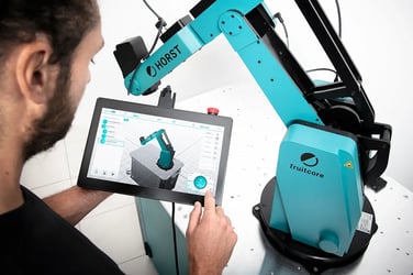 Ein Mann bedient das Panel des Industrieroboters HORST600 und der Roboter selbst ist im Hintergrund zu sehen.