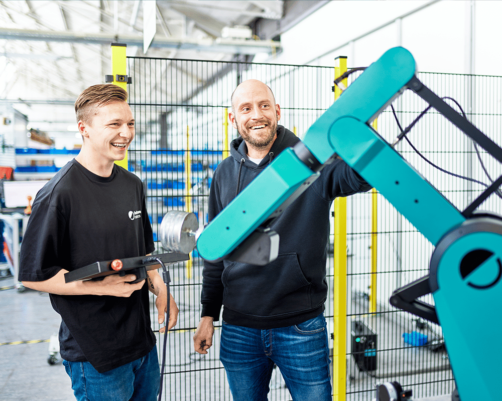 Zwei Männer stehen hinter einem HORST1400-Roboter. Einer hält ein Bedienfeld in der Hand.