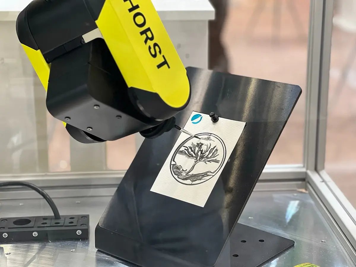 Der AI Robot Painter HORST 600 führt eine künstlerische Anwendung aus und zeichnet präzise ein Baum-Motiv auf ein Etikett aus Papier, das auf einer geneigten Halterung fixiert ist.
