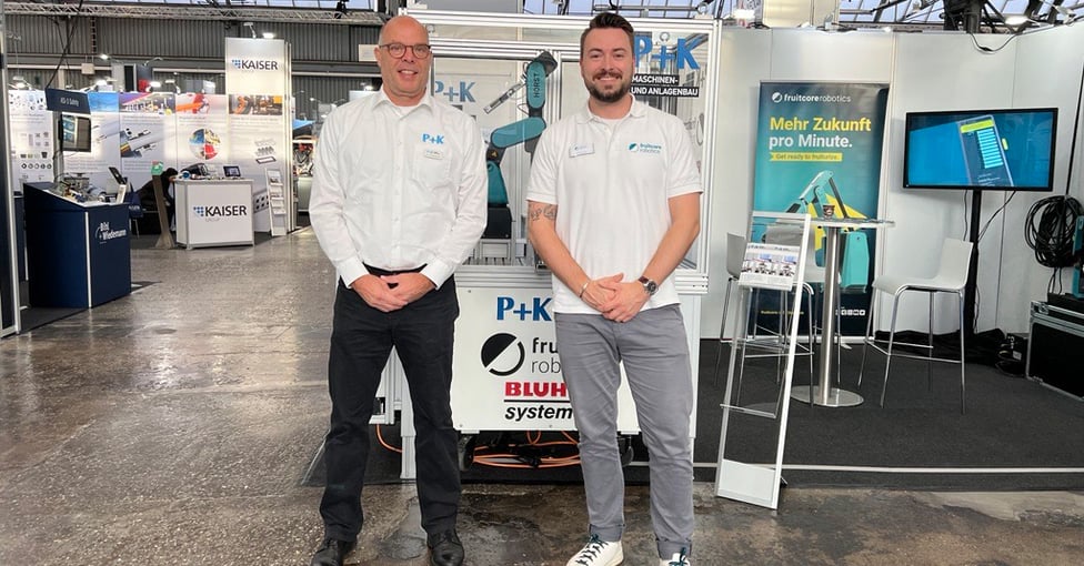 zwei Männer die vor einem Messestand stehen