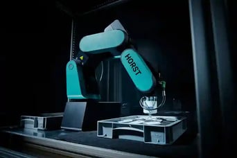 Ein HORST600 Roboter der in einer schwarzen Umgebung in eine Kiste greift 