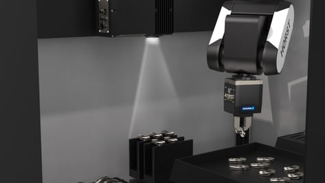 Ein HORST-Industrieroboter mit SCHUNK-Greifer nimmt ein zylindrisches Metallteil aus einem Sortiermodul auf, unterstützt durch gezielte Beleuchtung für visuelle Qualitätskontrolle und Pick-and-Place-Genauigkeit.